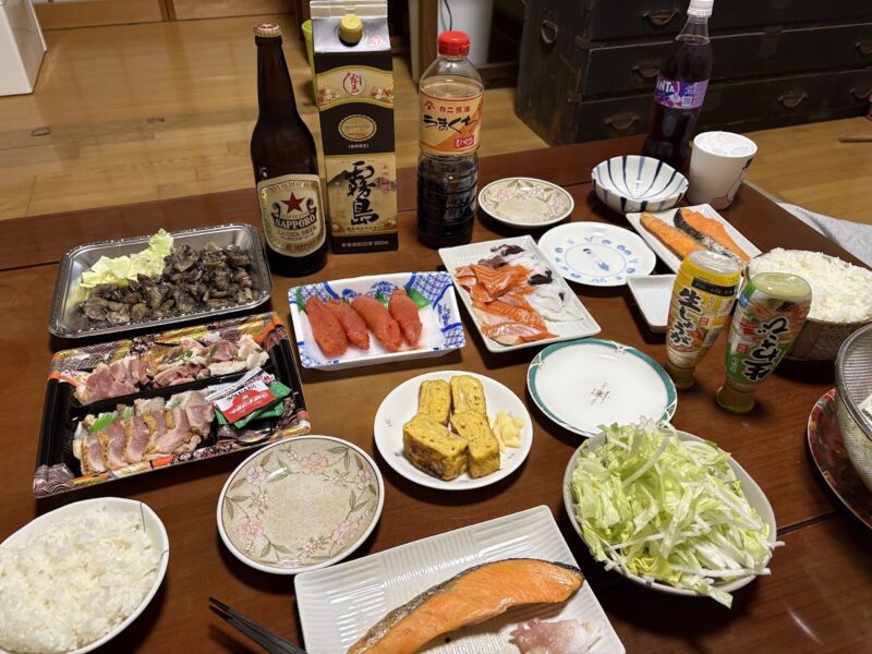 サーモンとイカの刺身、明太子、地鶏の炭火焼き、だし巻き卵が並ぶ晩酌の食卓